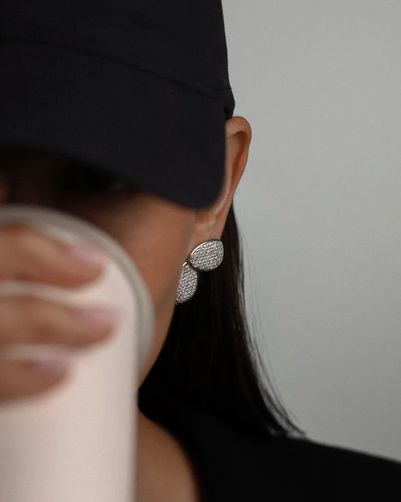 Sculptural pavé earrings visible beside a raised drink